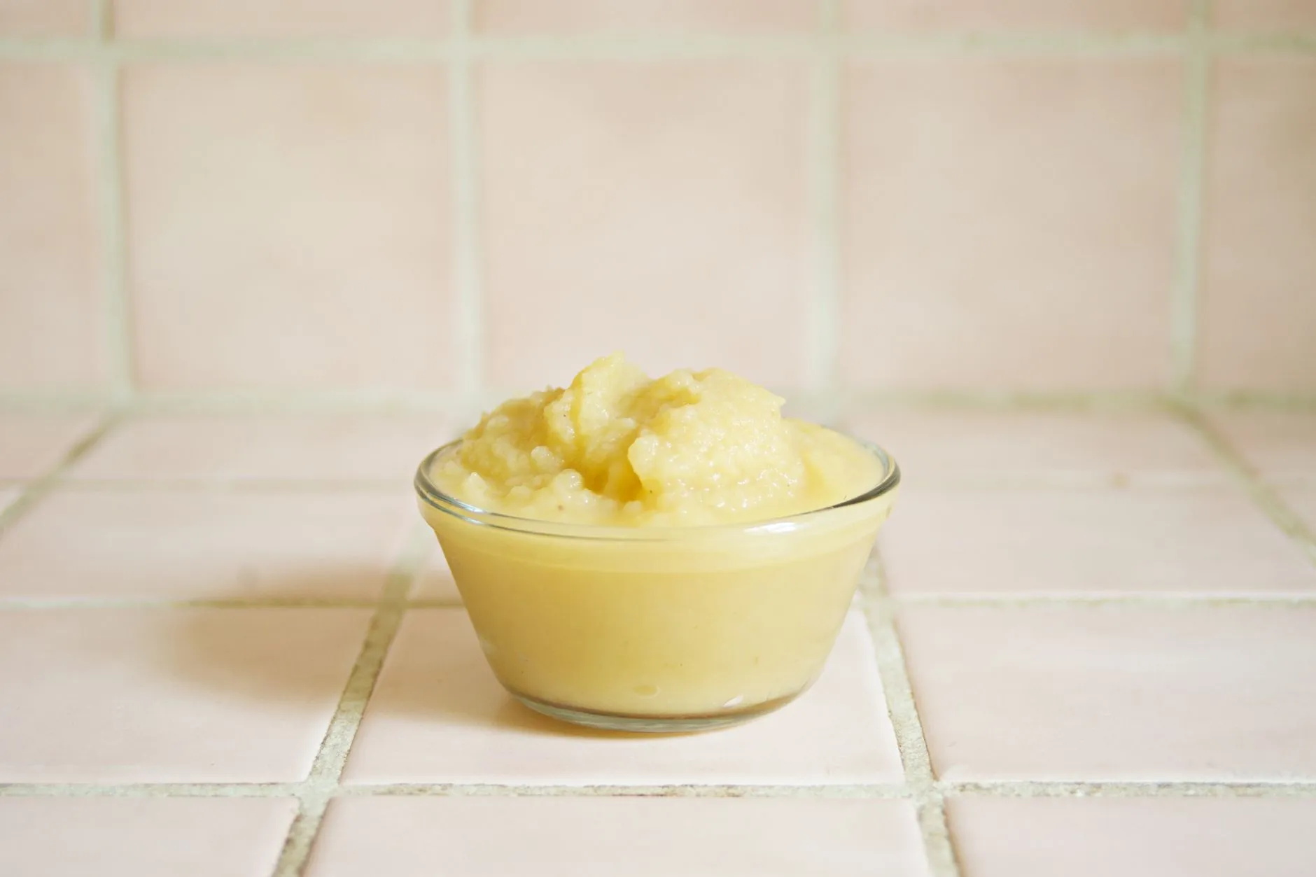 Close-up of homemade applesauce in a clear glass bowl on a tiled surface.
