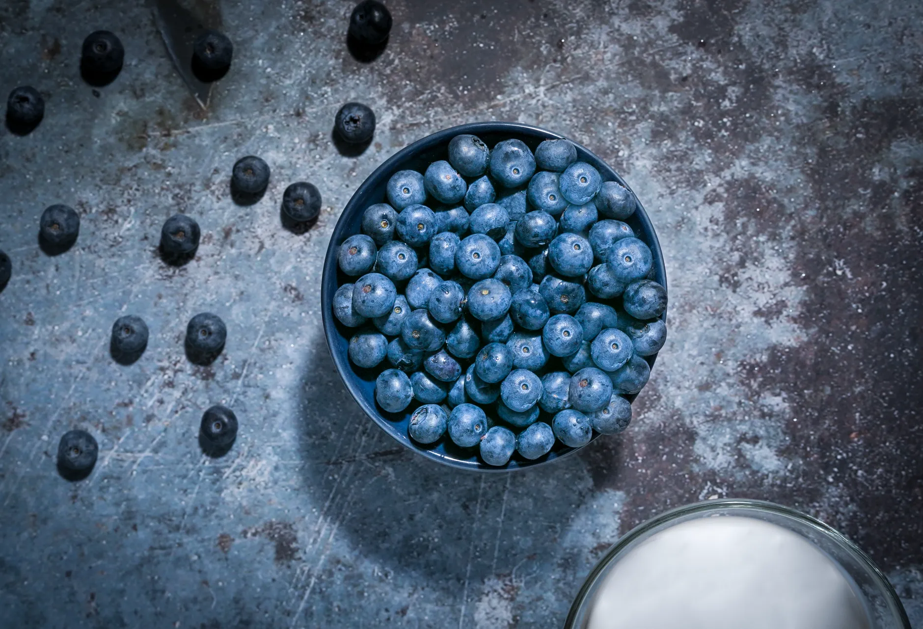 Top-down shot of fresh blueberries in a bowl on rustic surface with dramatic lighting.