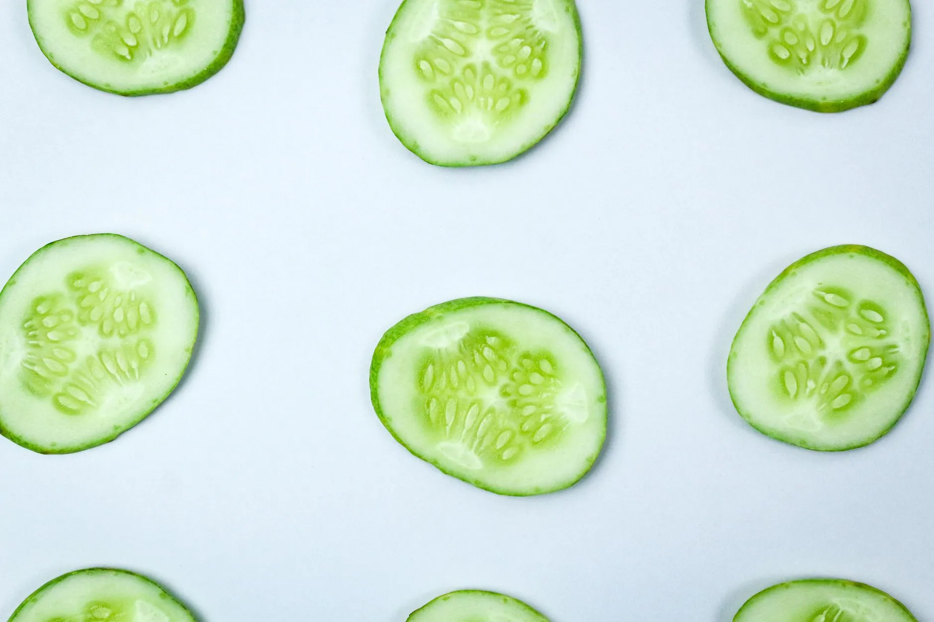 Close-up of fresh cucumber slices in a flatlay pattern on a white background.