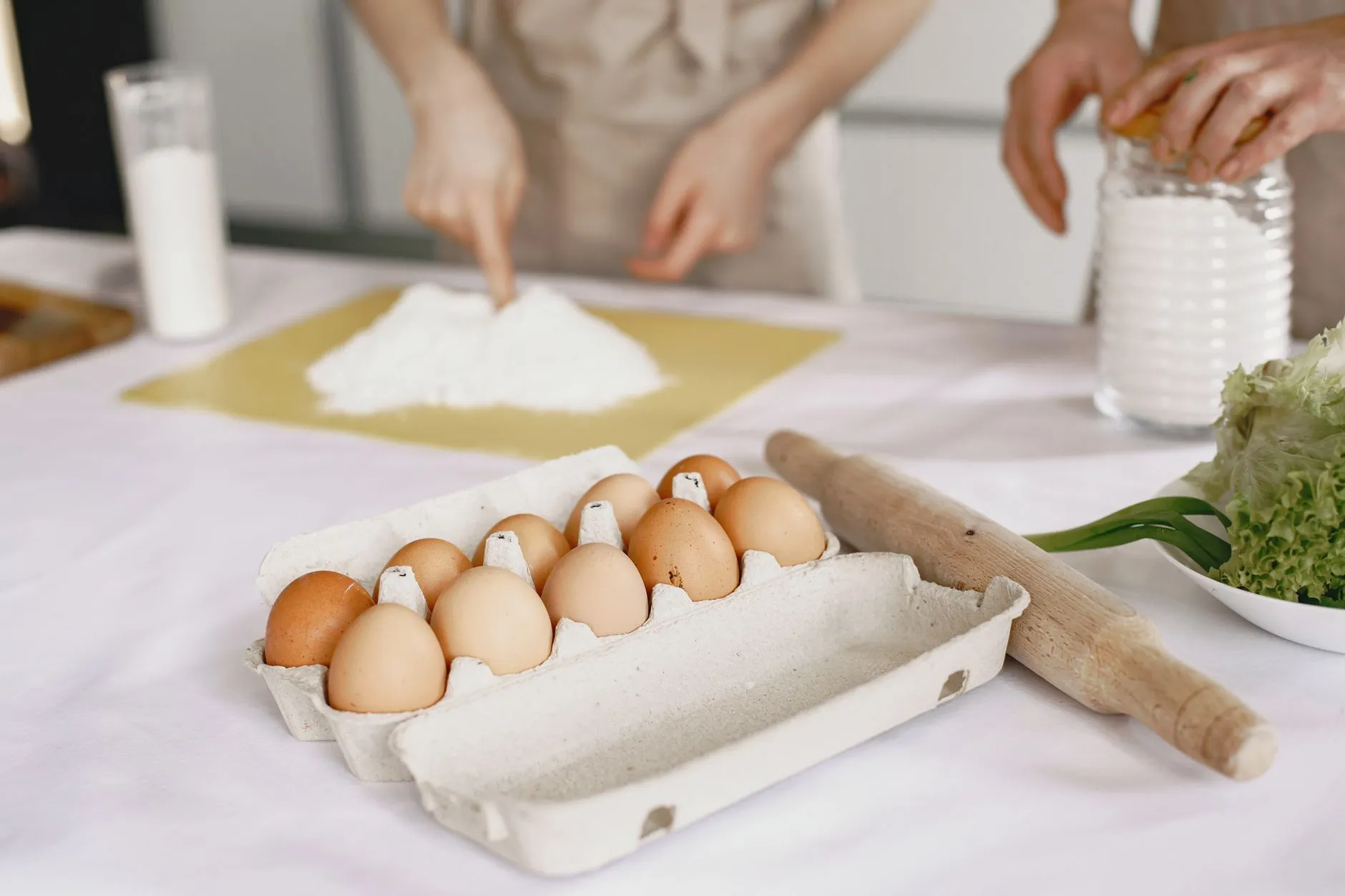 Brown eggs, flour, and a rolling pin on a kitchen table ready for baking.