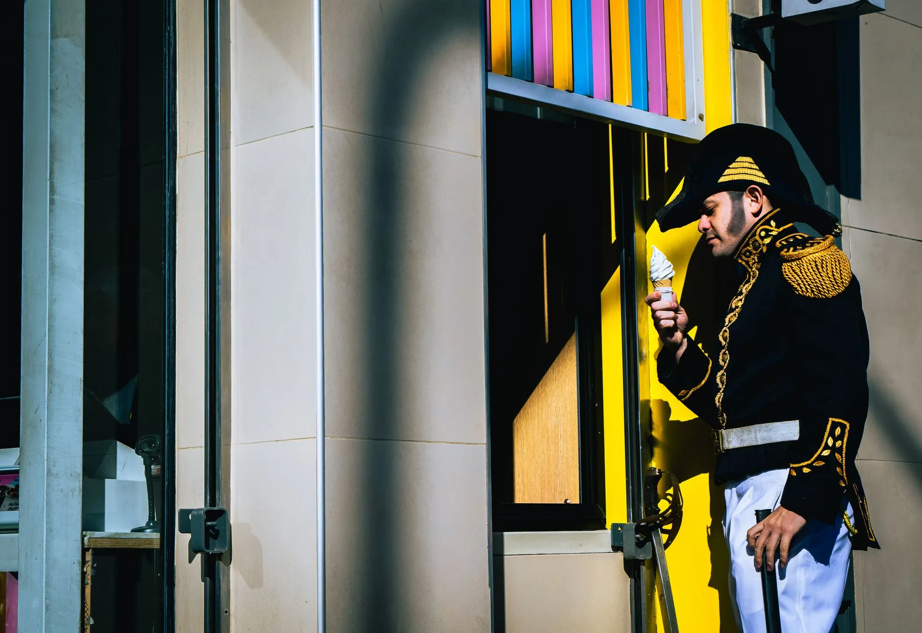 A man in a historical uniform enjoying an ice cream cone outside a colorful urban building.