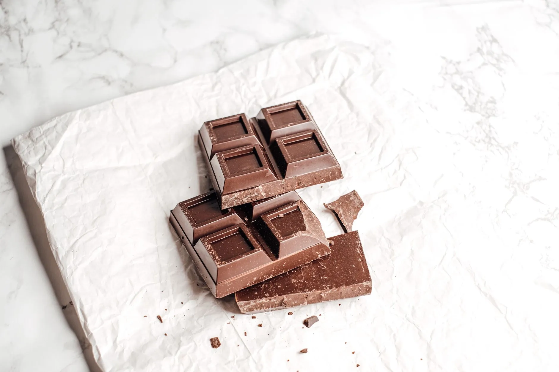 Close-up of dark chocolate bar on crumpled white paper, showcasing texture.