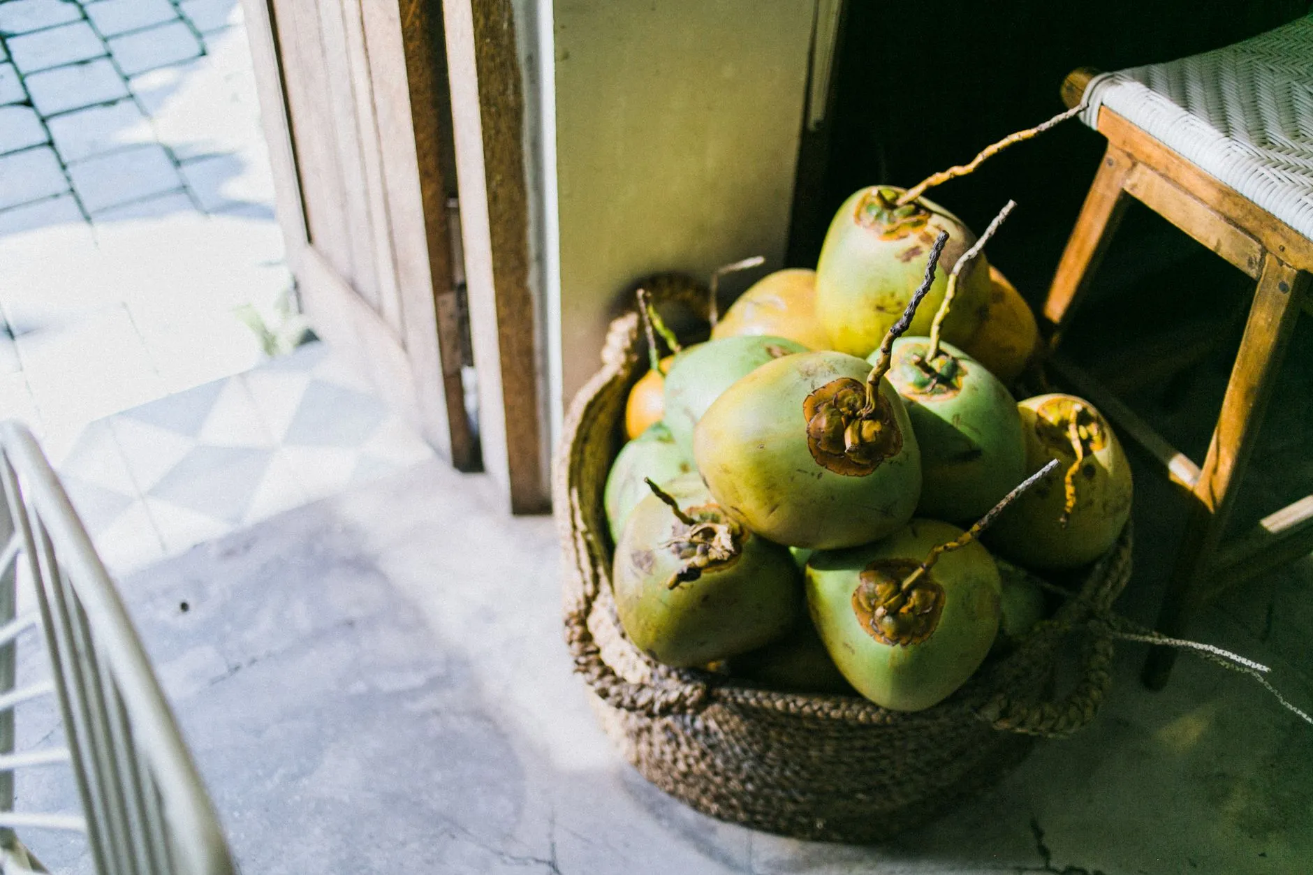 From above of young light green coconuts in fabric basket next to old wooden stool in daytime