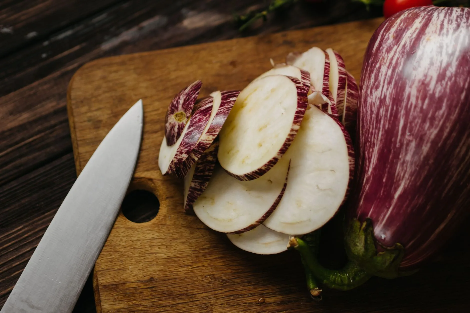 Freshly sliced eggplant on a wooden board with a knife, showcasing healthy cooking ingredients.