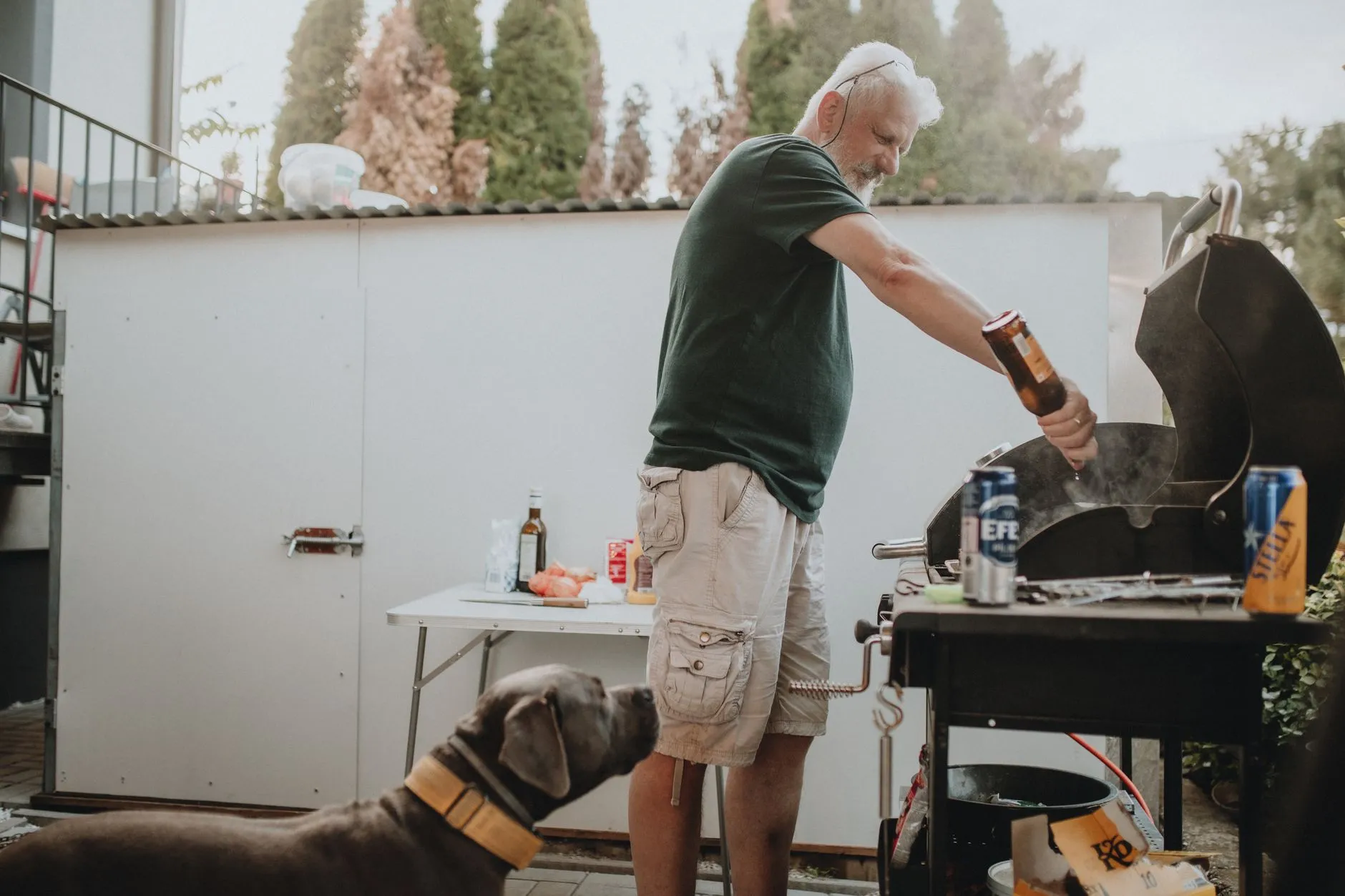 A man grilling outdoors with a dog nearby during a summer barbecue. Relaxed and casual setting.