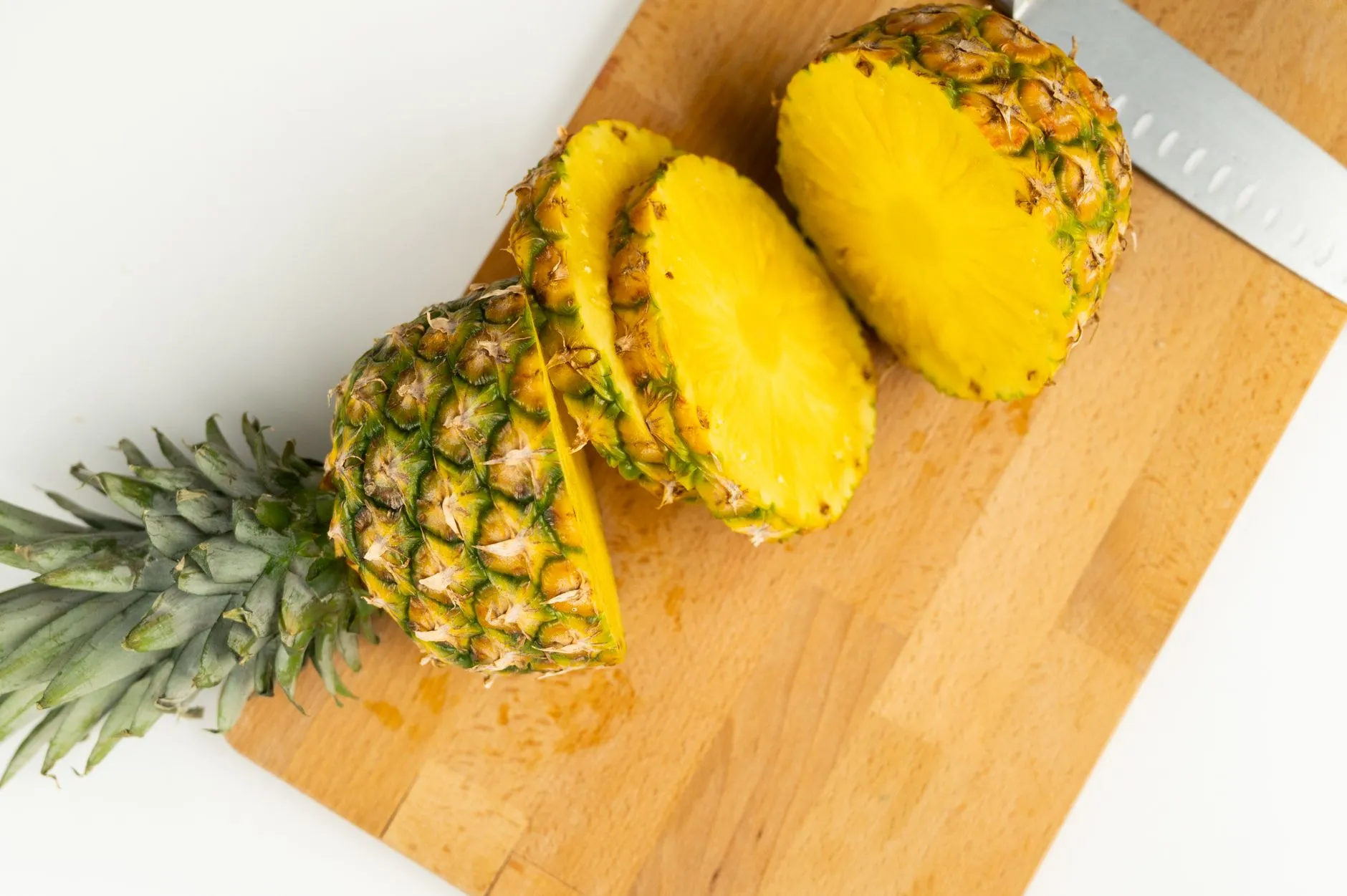 Overhead view of tasty cut pineapple pieces with leaves and juicy flesh on wooden cutting board