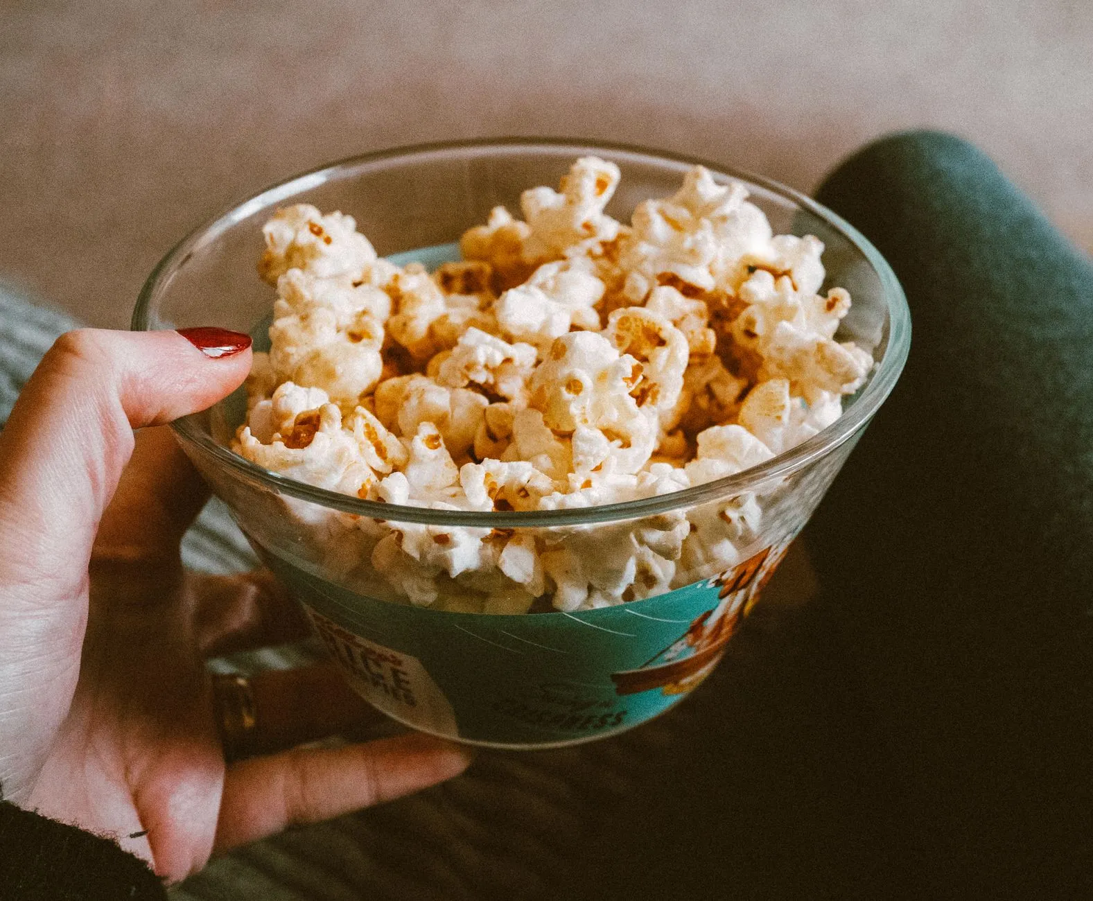 Close-up of a hand holding a glass bowl filled with delicious popcorn. Perfect snack time capture.