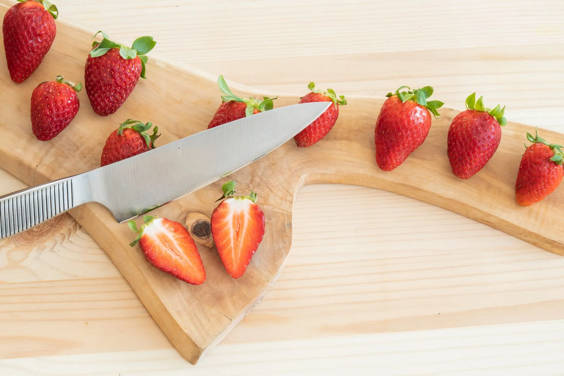 Sliced strawberries on a wooden chopping board with a knife, perfect for food-related projects.